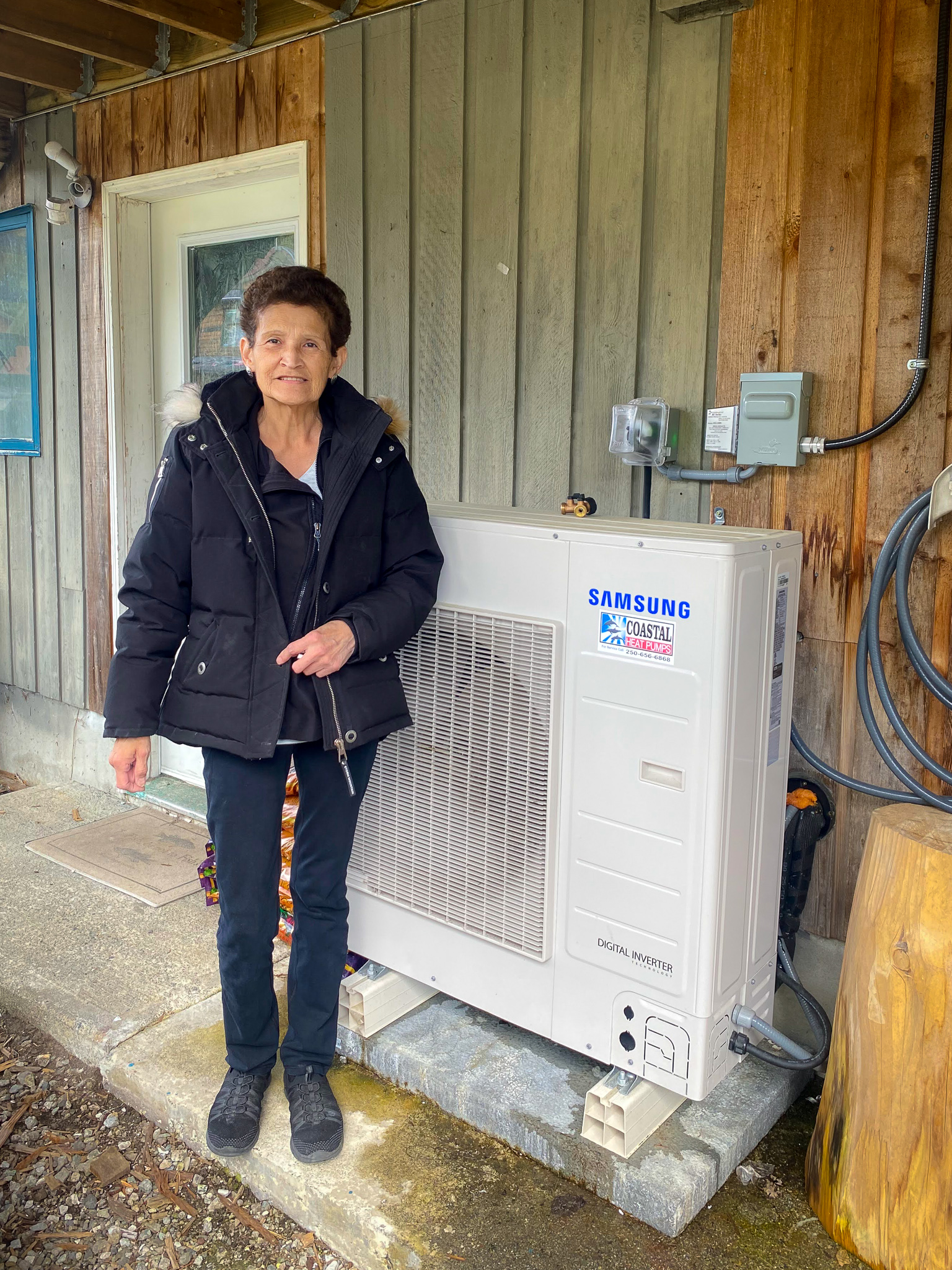 Haíɫzaqv Nation resident stands in front of her new heat pump.