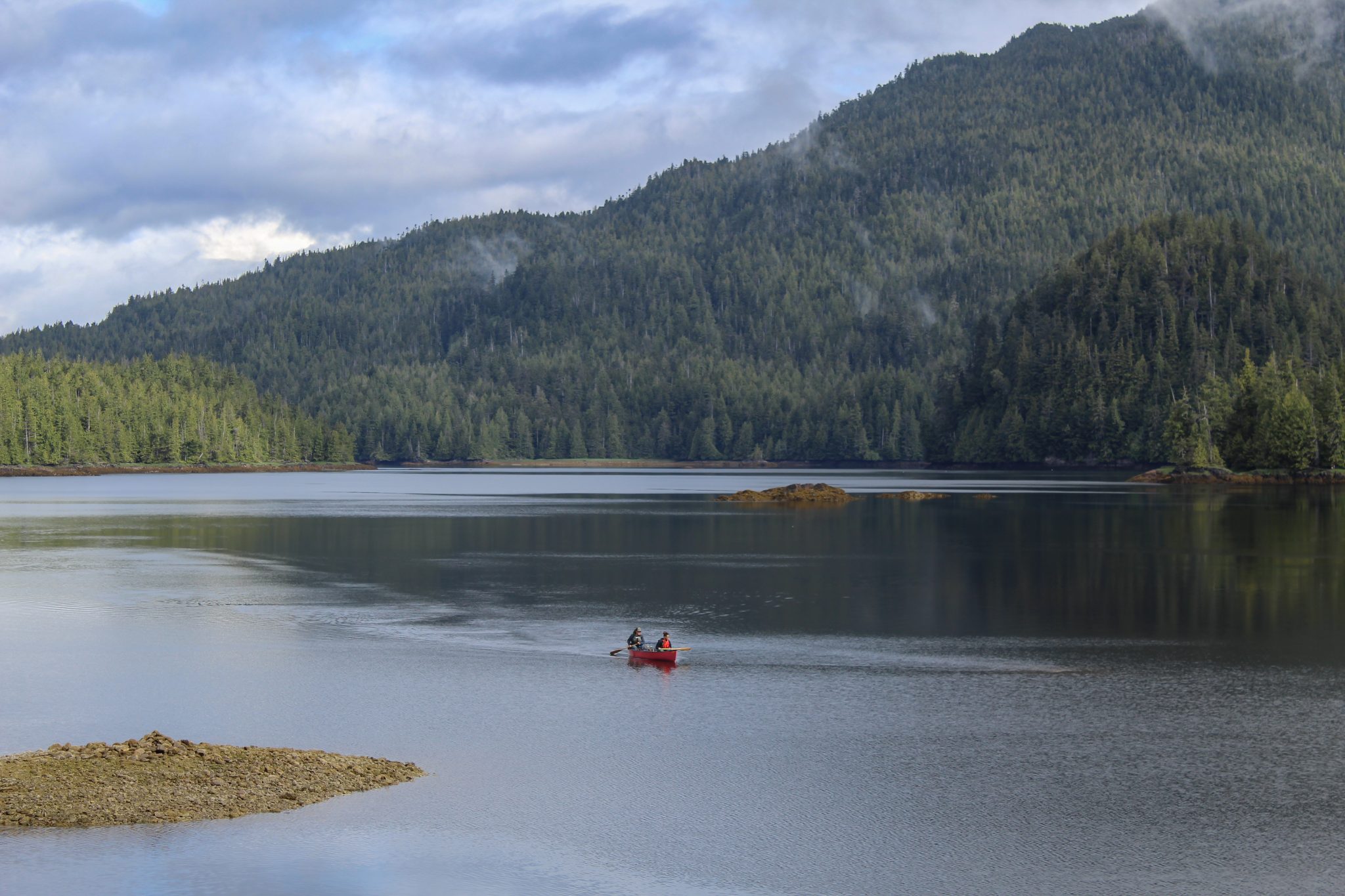 A teacher and student paddle a canoe. They are surrounded by green mountains.